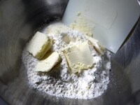 ホットケーキミックスに約2cmのスライスしたバターを入れ、カード（またはフォーク）で粉とまぶしながら、バターを切り刻みます。