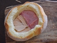 パンの内側にバターを塗ります。<br />
パンの底半分にハム２枚を、残りの半分にサラダチキン3-5枚ほど敷き詰めます。