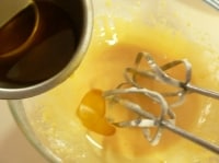ハンドミキサーで卵黄を軽く混ぜ、残りのグラニュー糖と塩を加えて白っぽくなるまで混ぜる。サラダ油を少しずつ加えながらしっかりと混ぜ、牛乳と水を加えてさらに混ぜる。<br />