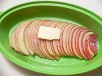りんごは芯をくり抜いて2mm厚に切り、斜めにずらして耐熱皿に並べる。グラニュー糖とレモン汁をふりかけ、バターをのせ、６００Wの電子レンジで3分～3分半加熱する。<br />