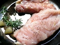 フライパンにオリーブオイル、叩きつぶしたニンニク、ローズマリー1枝、鶏肉を並べて焼きはじめる。鶏肉は皮を下にする。<br />