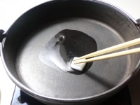 すき焼き鍋を火にかけ、牛脂を溶かして鍋全体に広げる。<br />