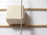 4～5cm角に切った豆腐をまな板にのせ、手前と向こう側に割り箸を置き、3mm幅ほどに包丁を入れていく。<br />