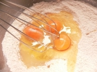 粉の中央に卵とレモン汁を入れ、泡立て器で初めに卵部分を混ぜ、周りの粉を取り込むように混ぜていく。<br />