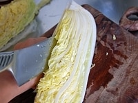 1/4にカットされた白菜を縦半分に切ります。にんにくは縦の薄切りにします。