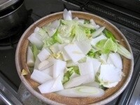 土鍋に昆布、食べやすい大きさに切った白菜、5cm幅程度に切った長ねぎ、短冊切りの大根の順に重ね、スライスしたニンニクと千切りのしょうがを散らし、塩をふりかける。