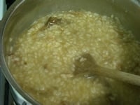 お米が鍋底にこびりついてきたら、コンソメと【1】の戻し汁を注ぎ入れ、塩をし、時々鍋底を返すようにしながら、リゾットを炊いていく。<br />