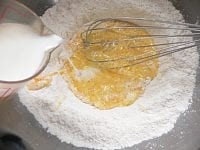 粉の真ん中に卵を割り入れ、牛乳を注ぎ入れ、泡だて器で混ぜる。<br />