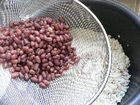 米を釜にあけ、ザルの上に小豆をあけて、ゆで汁だけを入れる。 <br />
<br />