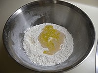 粉類と塩は合わせて一度ふるっておきます。ドライイースト、オリーブオイル、ぬるま湯(100ml)を混ぜ合わせ、粉の中央にくぼみを作り、少しずつ加え粉と混ぜ合わせます。<br />