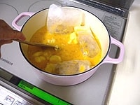 袋に入れたレモン皮を加え、バターと砂糖が溶けるまで弱火でかき混ぜながら煮ます。<br />