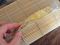 巻きすの上にラップを敷きます。そこへ、あつあつの卵焼きをのせて巻き、形を整えます。粗熱が取れたら、切り分けてできあがりです。<br />