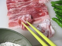 豚肉は1枚をくしゅっと箸でつまむようにしてまとめ、小麦粉を薄くまぶします。<br />
ししとうを使う場合は、包丁で縦に切り込みをいれます。