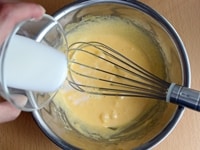 ボウルに卵黄を入れ、残り半量のグラニュー糖（45g）を入れ、もったりとするまで泡立て器で混ぜます。牛乳、バニラエッセンスをさらに加え、混ぜます。<br />