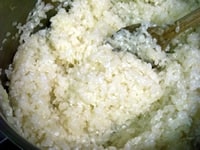 厚底深鍋にオリーブオイル、みじん切りのタマネギを入れ、中火にかけ、しんなりするまで炒めたら、軽く洗った米を入れ、水分がなくなるまで炒める。水分が飛んだら、コンソメ（ブロード）をゆっくりと回し入れる。