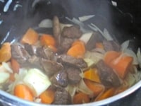肉をサラダ油を入れたフライパンで色づくまで炒め、野菜を入れた鍋に加える。<br />