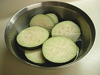 米茄子は2cm厚の輪切りにします。切り口に十文字に包丁を入れ、水にさらしてアク抜きをします。<br />