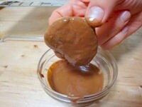 湯せんで溶かしたチョコレートを片面にたっぷりつけて、余分なチョコレートを落とします。<br />
